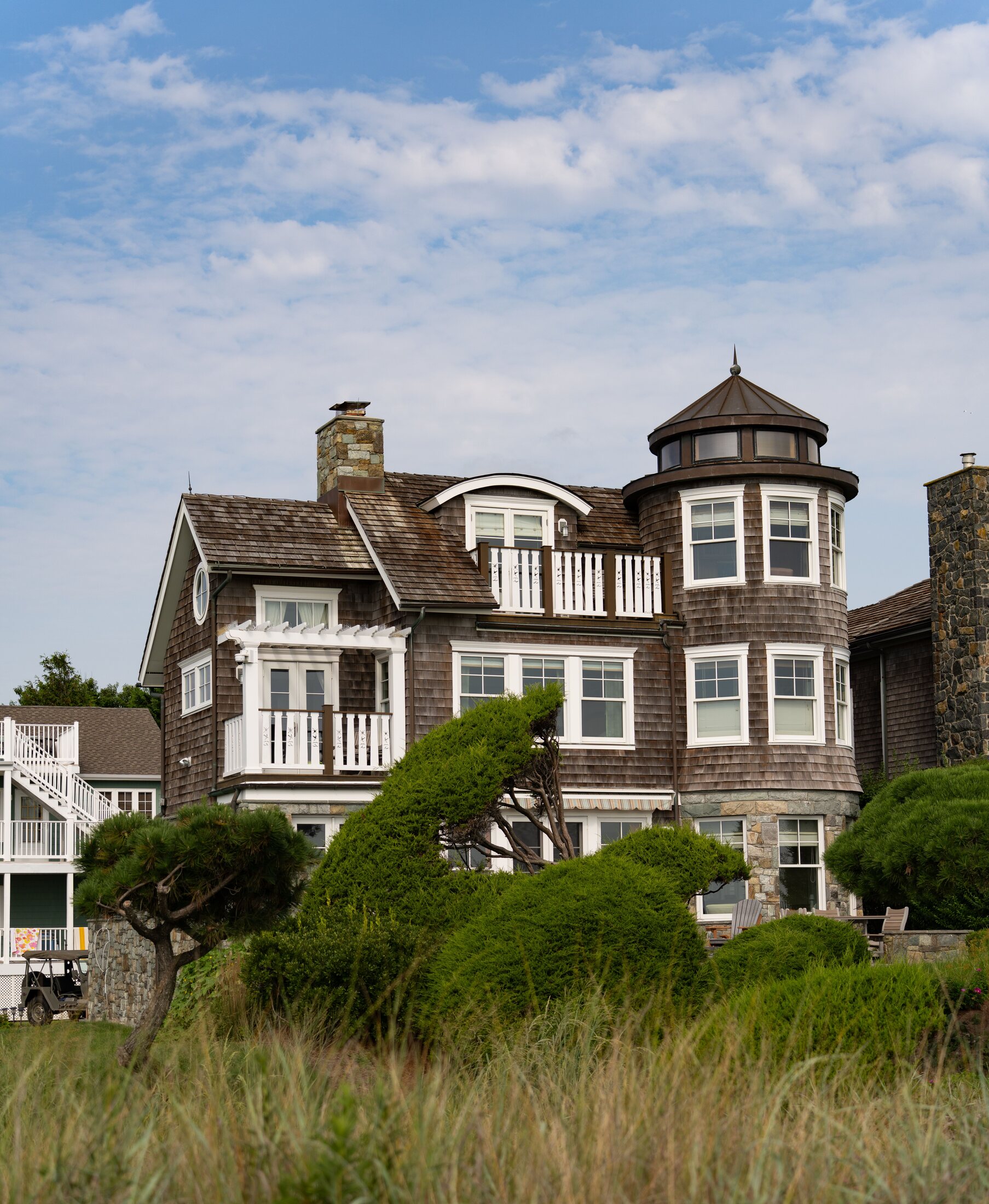A refined shingle-style coastal home framed by sculpted greenery and dune grass