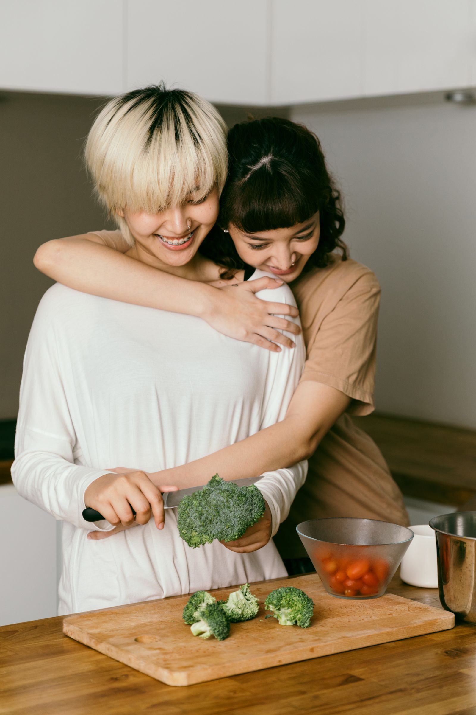 Two young housemates laughing together while preparing food in a sunny kitchen